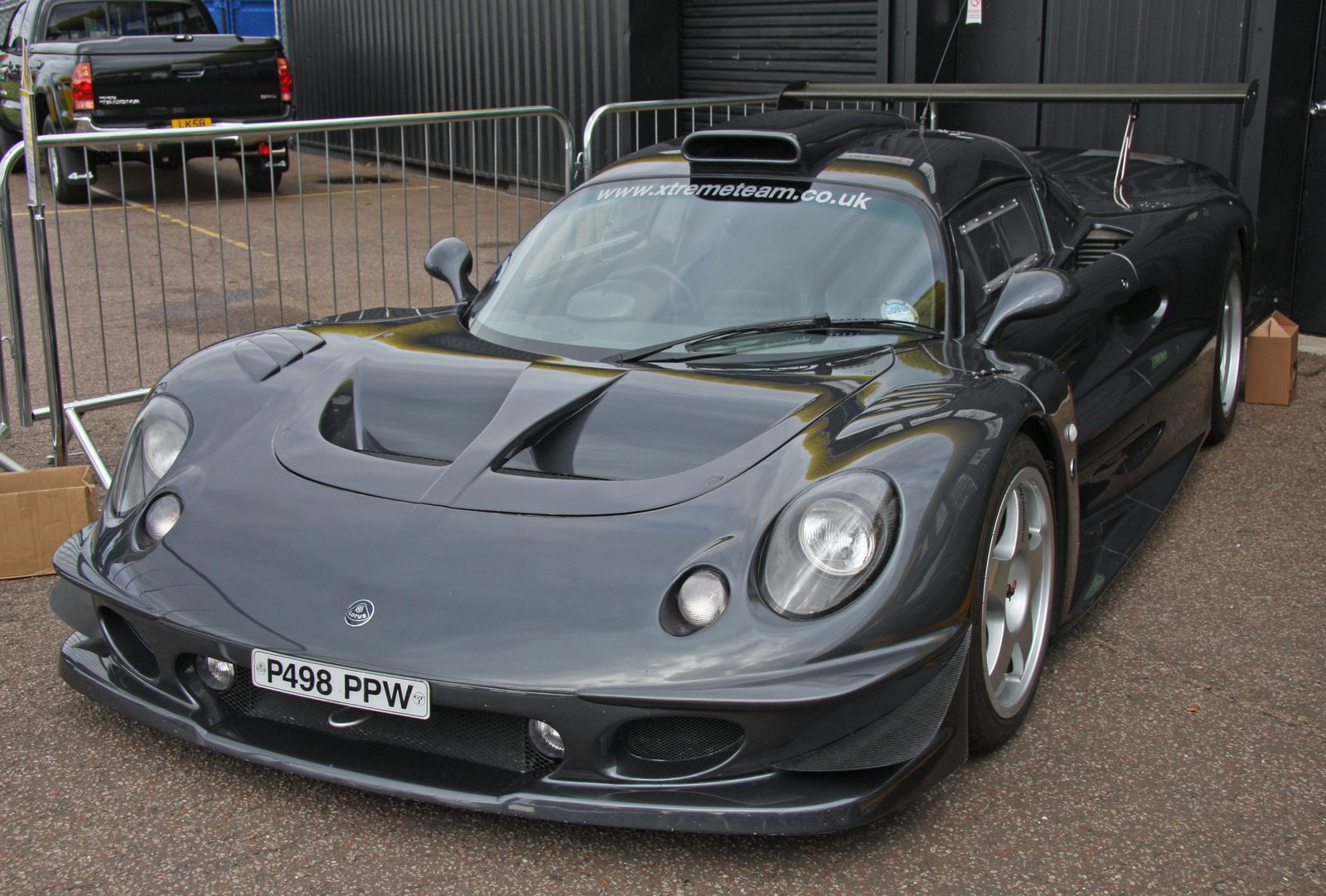 The Lotus Elise GT1 road car P498 PPW parked against a paddock barrier, seen from the front three-quarter.